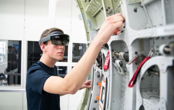 10 July 2019, Hamburg: During a demonstration, an Airbus trainee shows the use of data goggles (Microsoft Hololens) on an aircraft component. The spectacles work with the "Mira Mixed Reality" application developed by Airbus and are used, among other things, in maintenance and installation. At an event on the Airbus premises, the Hamburg Chamber of Commerce presented a position paper on digital education. Photo: Daniel Reinhardt/dpa (Photo by Daniel Reinhardt/picture alliance via Getty Images)