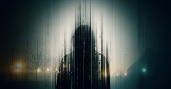 A double exposure of a Silhouette of a mysterious hooded figure without a face, in a city at night.