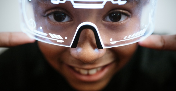 A child wearing an augmented reality headset or goggles smiles at the camera. Metaverse and safe space concept.