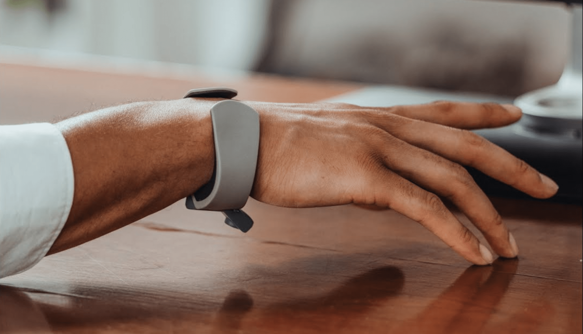 Eine Hand mit TapXR-Armband tippt auf der Schreibtischplatte.