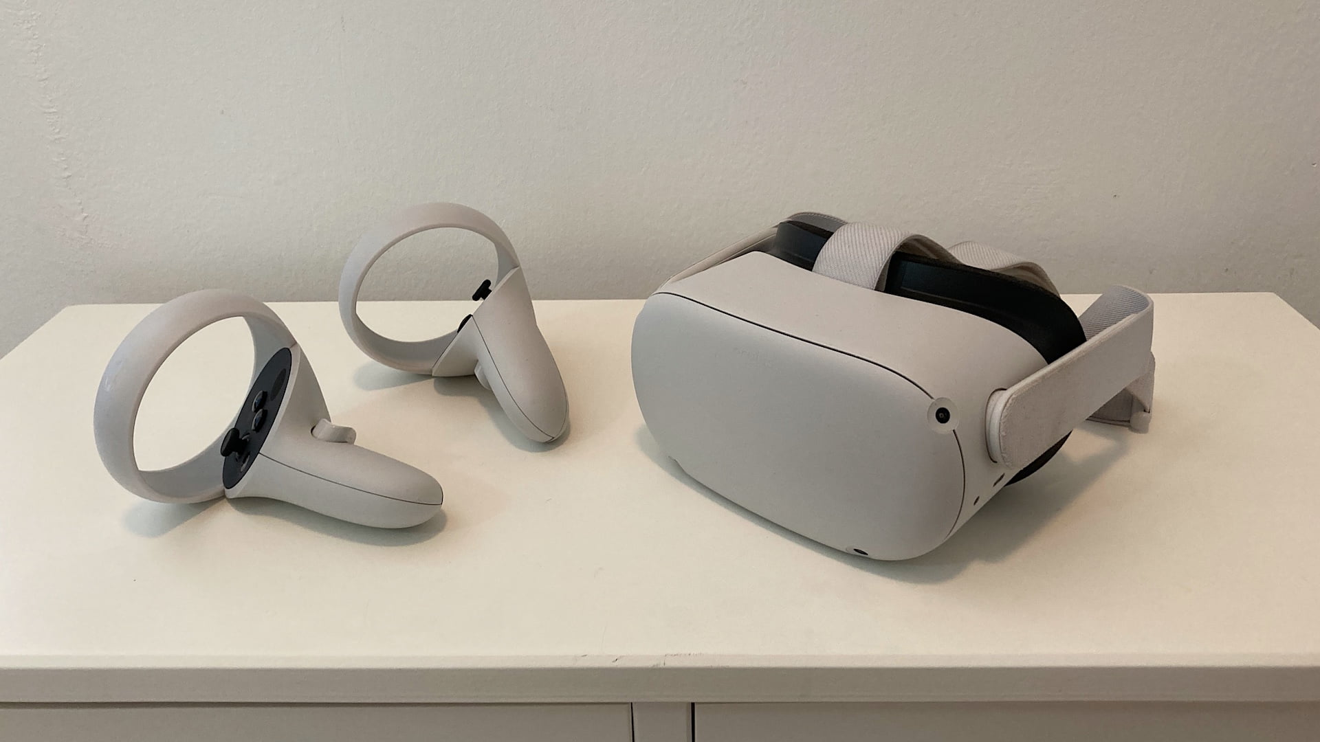 Eine Quest 2 liegt neben den zwei Touch-Controllern auf einer Kommode.